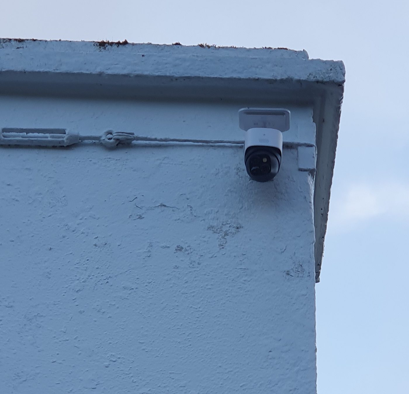 Security camera on a white wall under the roof edge